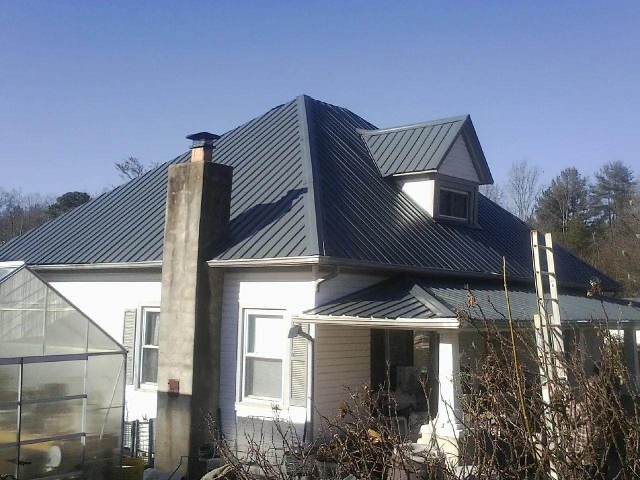 Dark blue standing seam metal roof on a white farmhouse with dormer — Slate & Tile Roof Repair by Roofing Brothers in Colusa