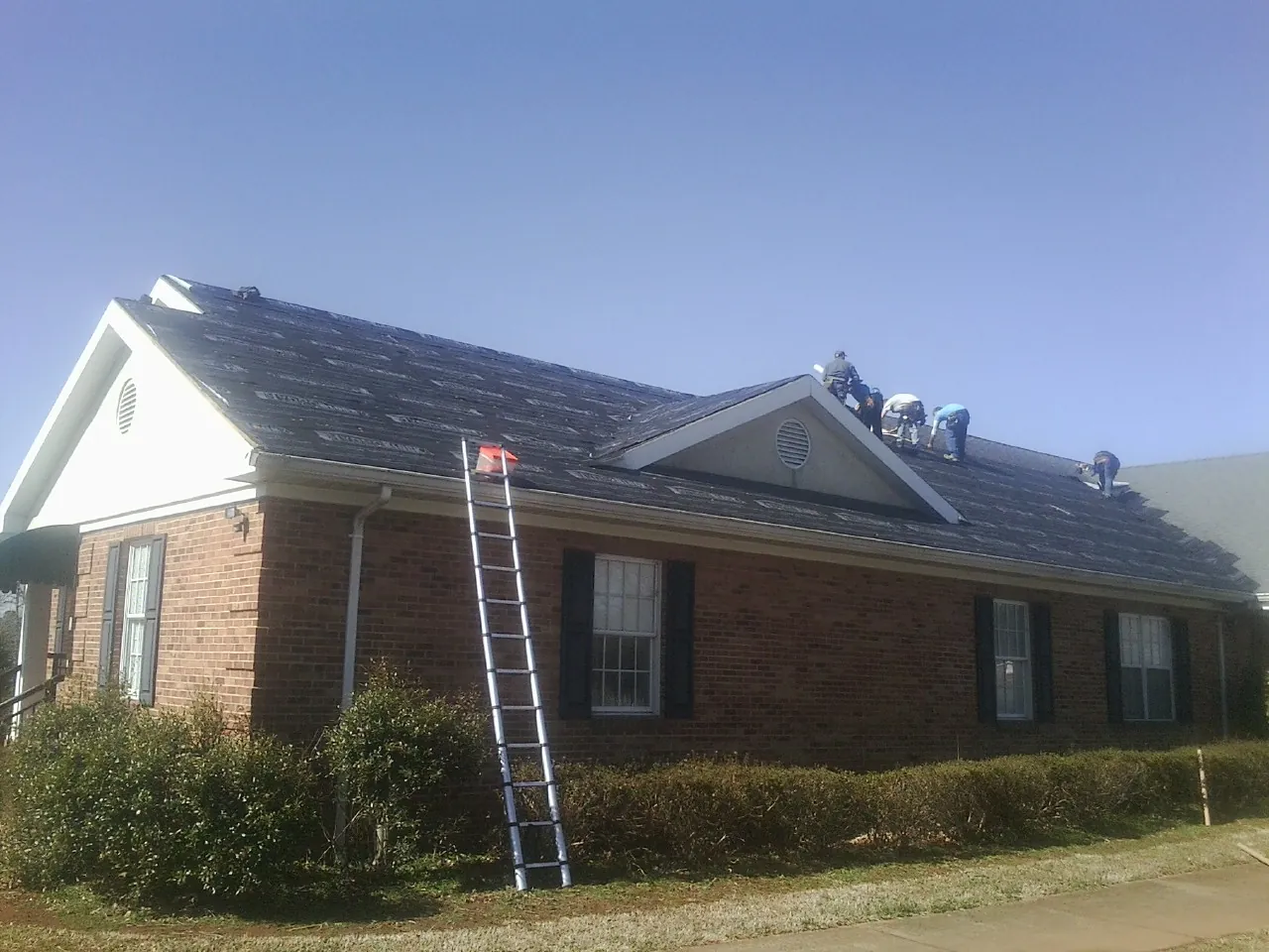 Crew tearing shingles off a brick ranch roof with a ladder set — Emergency Roof Repair work by our crew in Colusa