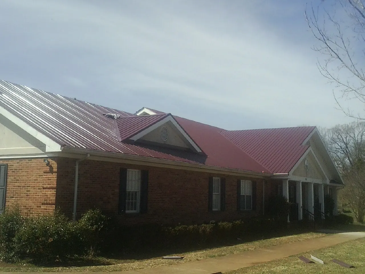 Red metal roof with gabled entries on a long brick building, from a Hail Damage Roof Repair job in Colusa