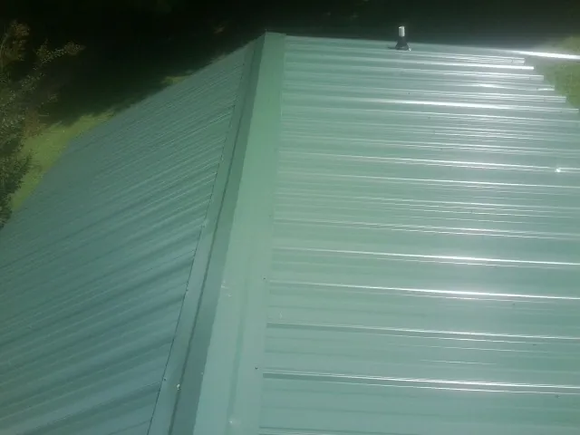 New green metal panels meeting at the ridge of a roof — Flat Roof Repair work by our crew in Colusa