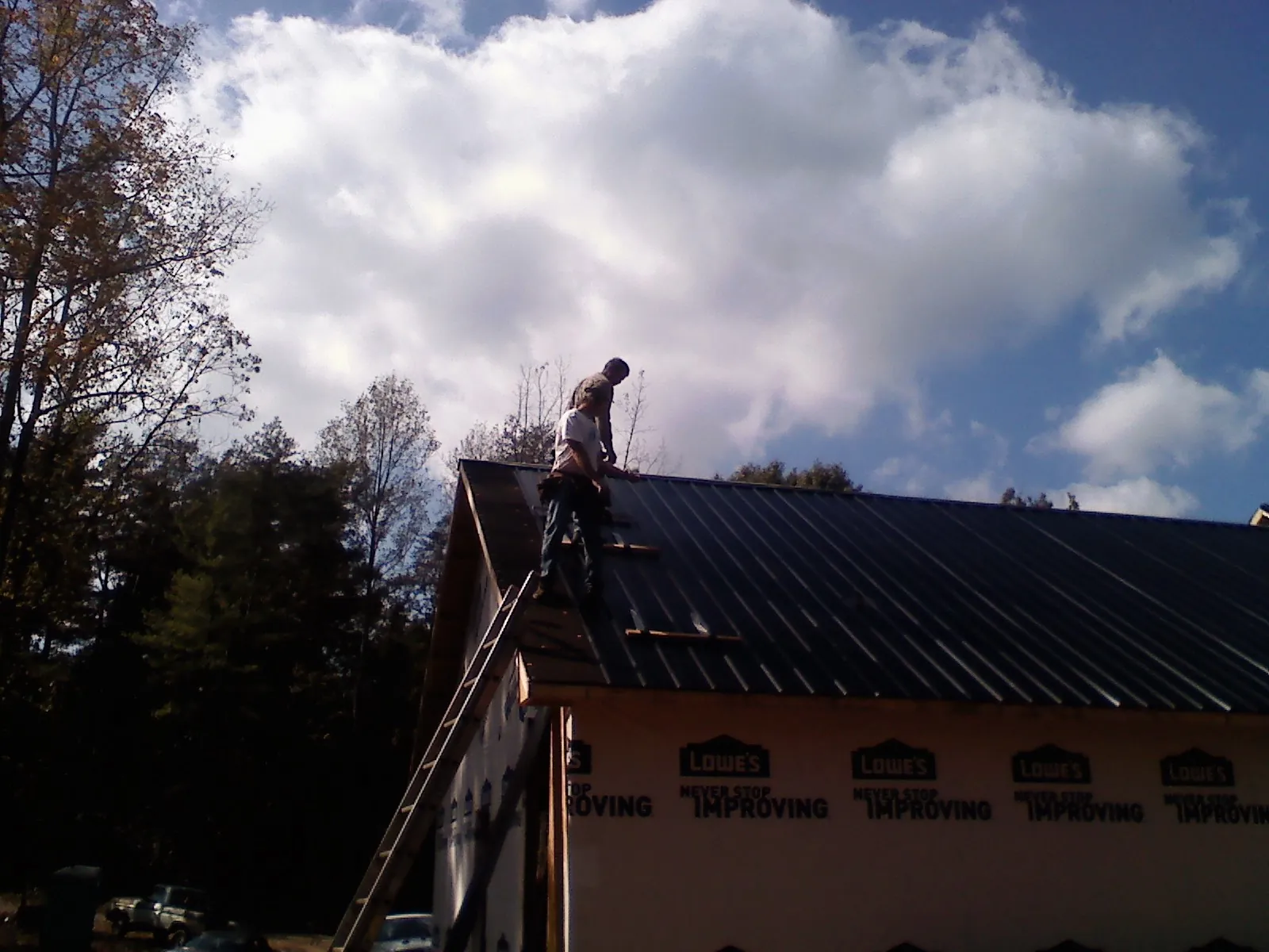 Roofer fastening dark metal panels high against a cloudy sky, from a Roof Inspection job in Colusa