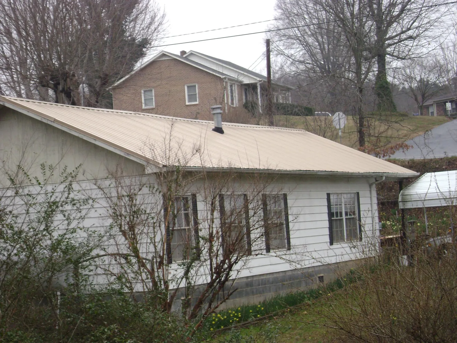 Tan metal roof on a white sided house set into a hillside — Commercial Roofing by Roofing Brothers in Colusa